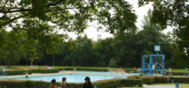 Außenschwimmbecken mit Bademeister Haus und Liegewiese mit Bäumen drum herum