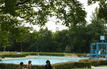 Außenschwimmbecken mit Bademeister Haus und Liegewiese mit Bäumen drum herum